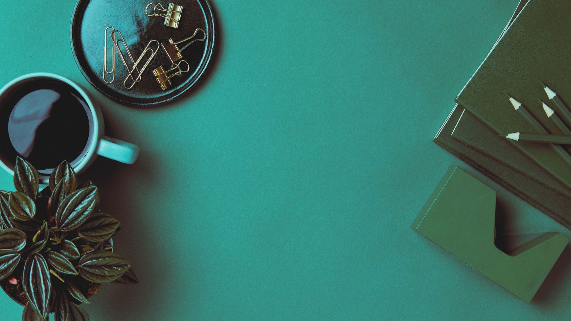 A stylish workspace setup featuring a cup of coffee, a plant, pencils lined on a notebook, and paper clips on a leather coaster - tools ready for taking a digital transformation assessment quiz.